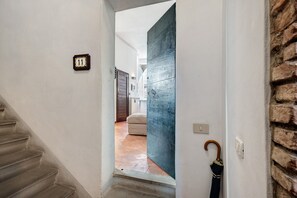 Ein Flur mit Nummernschild, einer Holztür, einer Treppe und einer Ziegelwand.
