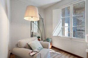 Ein Zimmer mit einer Couch, einer Lampe, einem Spiegel, einem Fenster und einem Blumentopf.