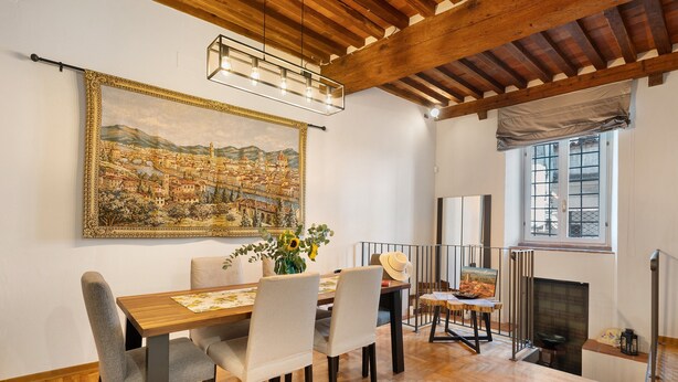A dining area with a wooden table, chairs, and a cityscape painting on the wall. - Apartment "Casa Conrad - Lucca" with Wi-Fi and Air Conditioning (Lucca)