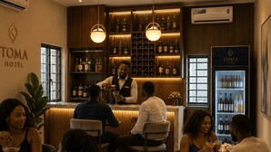 Zona de bar con un cantinero, enfriador de vino y clientes sentados en mesas.