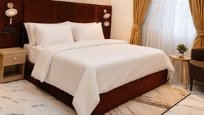 Habitación de hotel con una cama grande, cabecera de madera, mesita de noche, una pequeña mesa con una planta y un lámpara en el techo.