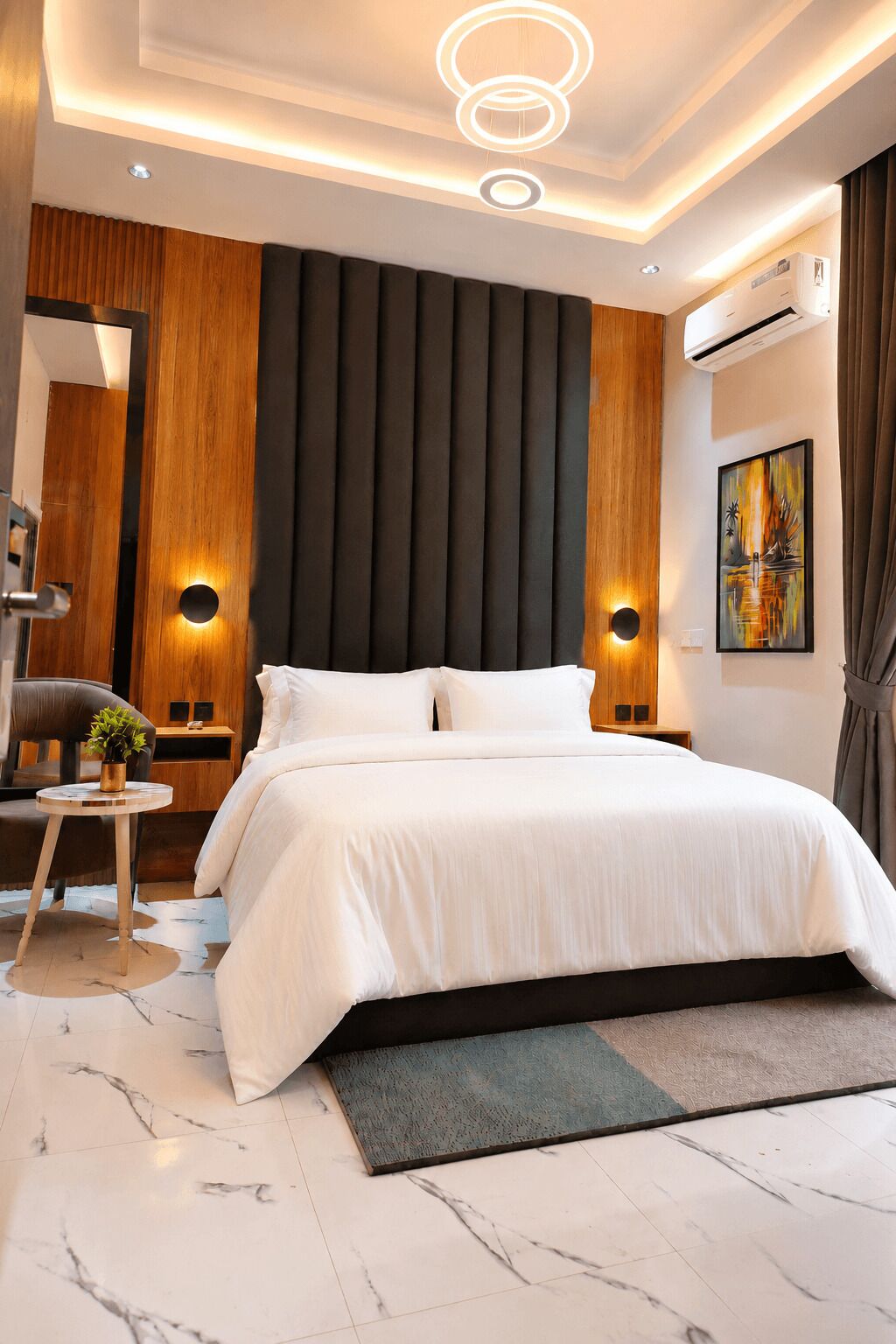 A modern bedroom with a large bed, wooden panel wall, and a ceiling light fixture.
