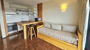 A compact living space with a kitchenette, wooden stools, a sofa, and a wall-mounted light fixture. - Lake and City steps from the Centro Civicoc (San Carlos de Bariloche)