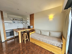 A compact living space with a kitchenette, wooden stools, a sofa, and a wall-mounted light fixture. - Lake and City steps from the Centro Civicoc (San Carlos de Bariloche)