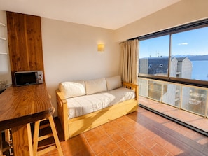 A room with a wooden sofa, a small table, and a view of a body of water through large windows. - Lake and City steps from the Centro Civicoc (San Carlos de Bariloche)