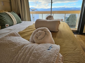 A hotel room with a bed, two rolled towels, a view of mountains through a window, and a balcony. - Lake and City steps from the Centro Civicoc (San Carlos de Bariloche)