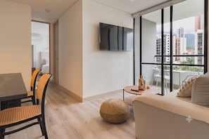 A modern living room with a sofa, a dining table with chairs, a TV mounted on the wall, and a large window with a city view. - ENZO Privé | Grand - Exclusive Corporate Suite in Medellín (Medellín)
