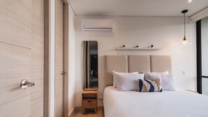 Ein modernes Schlafzimmer mit einem großen Bett, einem Schminkspiegel, einem kleinen Nachttisch aus Holz und einer Wand-Klimaanlage.