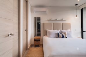 A modern bedroom with a large bed, a bedside mirror, a small wooden nightstand, and a wall-mounted air conditioning unit. - ENZO Privé | Grand - Exclusive Corporate Suite in Medellín (Medellín)