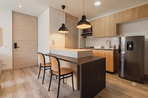 A modern kitchen with a central island, two pendant lights, a built-in stove, and a stainless steel refrigerator. - ENZO Privé | Grand - Exclusive Corporate Suite in Medellín (Medellín)