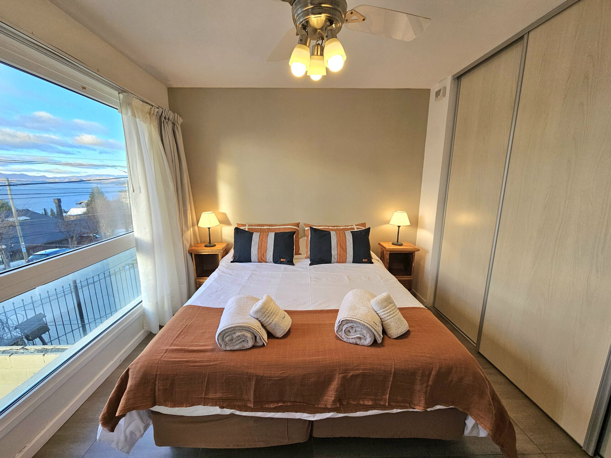 Habitación de hotel con una cama grande, dos lámparas de noche, un ventilador de techo y vistas al exterior.