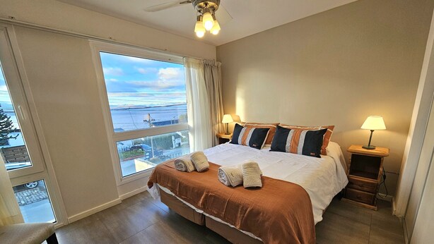 Camera d'albergo con un letto grande, due lampade sui comodini, una ventola a soffitto e vista all'esterno attraverso un'ampia finestra.