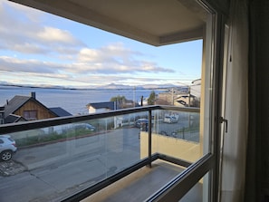 Ein Balkon mit Blick auf eine Straße, parkende Autos und ein ferner Bergpanorama.