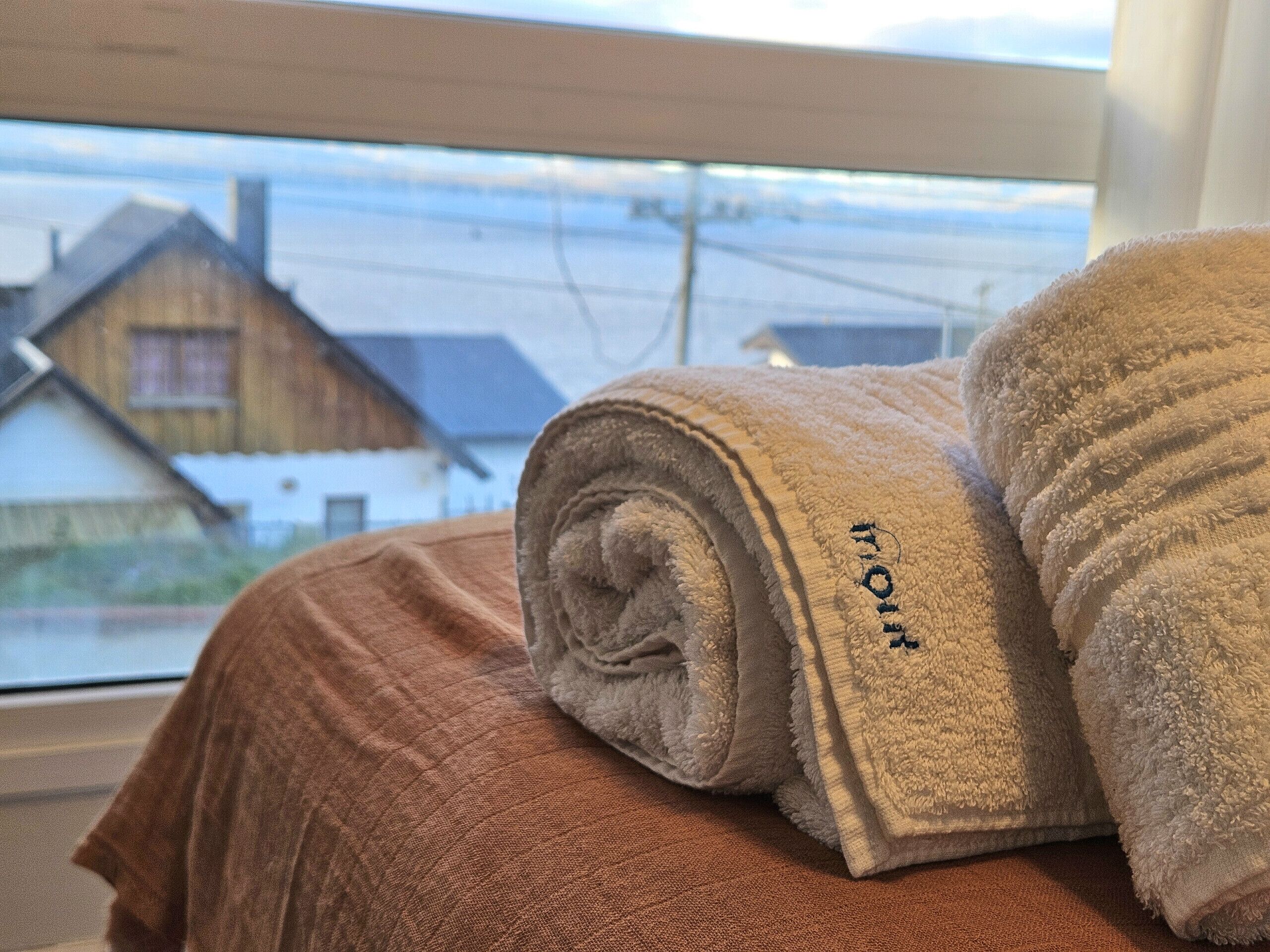 A bed with a brown blanket and two rolled towels with embroidered text.