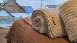 Un letto con una coperta marrone e due asciugamani arrotolati con ricami.