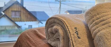 A bed with a brown blanket and two rolled towels with embroidered text.