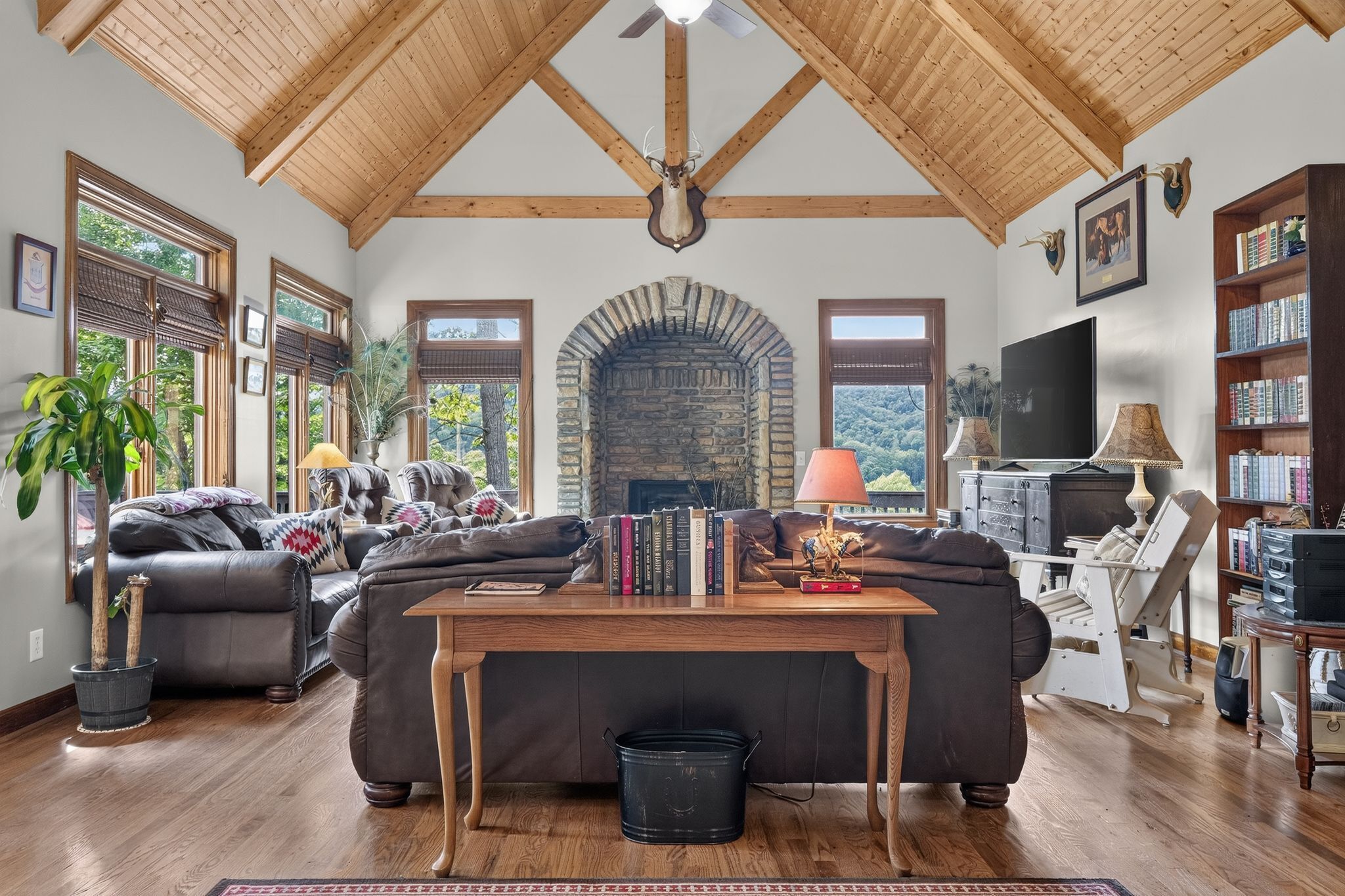 A spacious living room with a stone fireplace, leather sofas, a wooden coffee table, and a television.