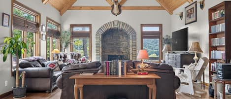 A spacious living room with a stone fireplace, leather sofas, a wooden coffee table, and a television.