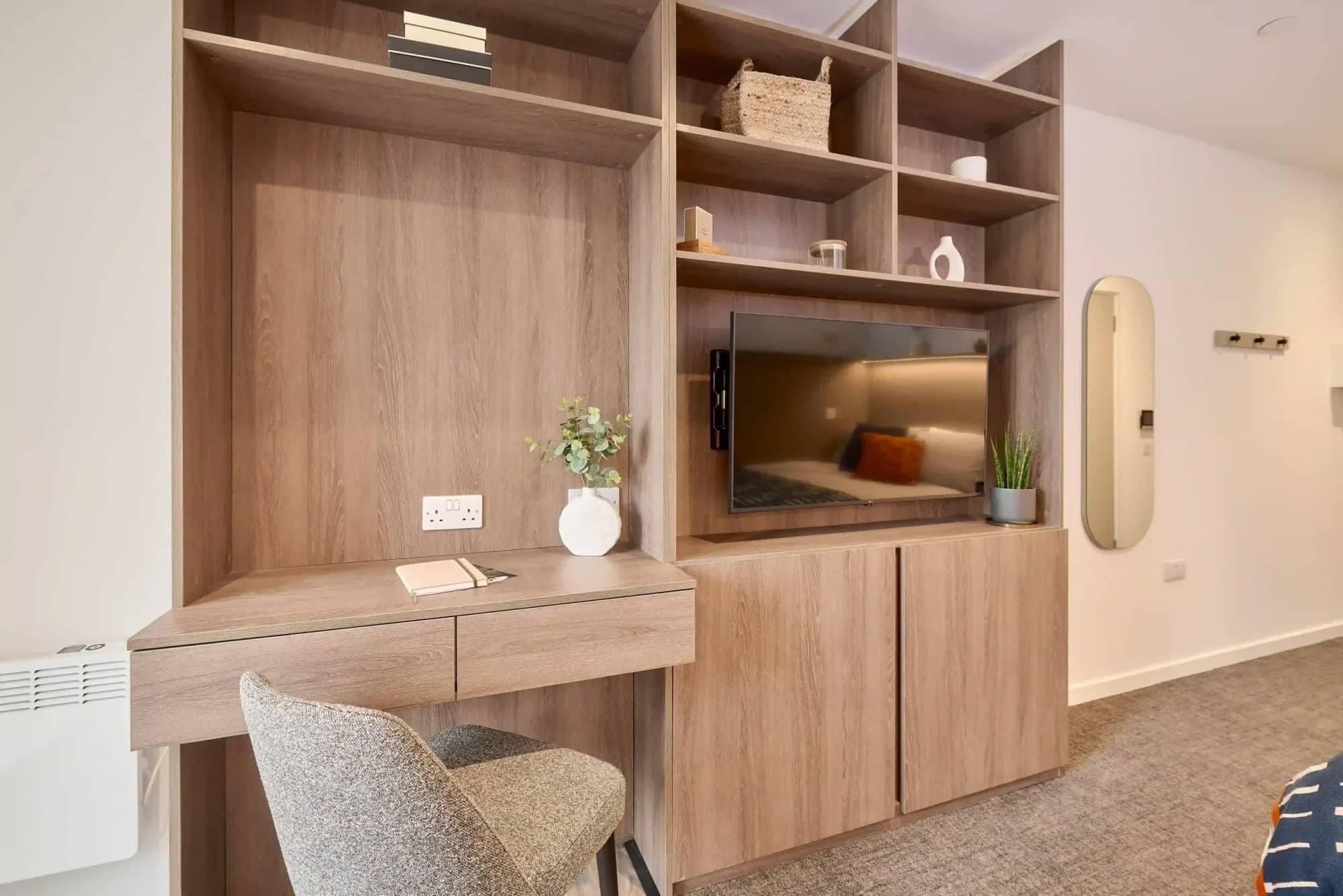 Una habitación moderna con escritorio integrado, televisión de pantalla plana y zona de estar con silla y cojines.