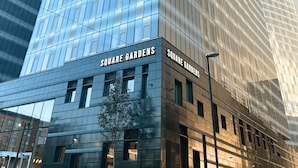 A modern building with a glass facade and the name 'SQUARE GARDENS' on the lower level. - Student Only Square Gardens Acer (Manchester)