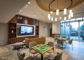 Eine Lobby mit Billardtisch, gemütlicher Sitzgelegenheit, einem großen Bildschirm und Blick durch die Glastüren.