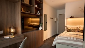 A modern bedroom with a bed, a desk with a lamp, and built-in shelving. - Student Only Square Gardens Acer (Manchester)