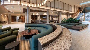 A spacious lobby with a curved seating area, a staircase, and a large window allowing natural light. - Student Only Square Gardens Acer (Manchester)