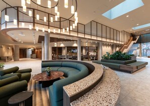 Eine geräumige Lobby mit einer gebogenen Sitzecke, einer Treppe und einem großen Fenster, das natürliches Licht hereinlässt.