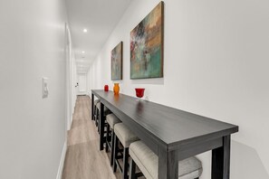 Ein Flur mit einem langen Esstisch, Barhocker und zwei Bildern an der Wand.