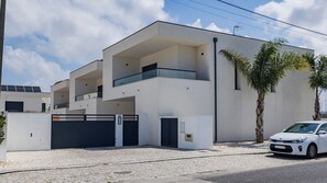 Ein modernes, zweistöckiges Gebäude mit Flachdach, einem Balkon im oberen Stockwerk und einem befestigten Eingangsbereich.