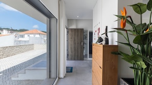 Ein modernes Interieur mit einer großen Schiebeglastür, die auf einen Balkon führt, einem Holzschrank mit Dekoration und einer Pflanze mit großen Blättern.