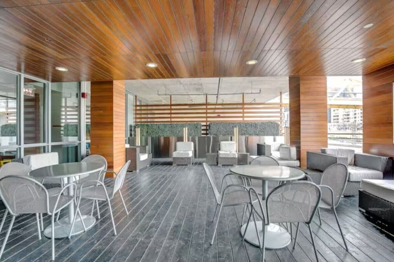 A modern indoor space with wooden ceiling panels, round tables, and grey chairs.