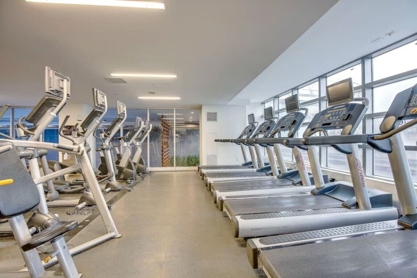 A gym with multiple treadmills and exercise equipment, large windows, and a clean, modern design.
