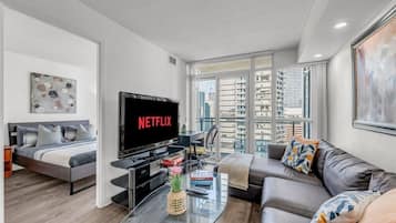 A modern living room with a bed, a sofa, a TV, and a glass coffee table.