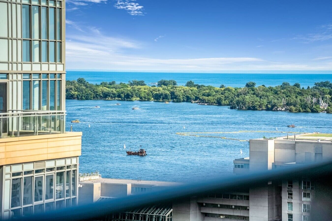 A view of a body of water with boats, a forested island, and modern buildings in the foreground.