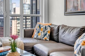 Ein modernes Wohnzimmer mit einem Ledersofa, einem gemusterten Sitzkissen und Blick auf die Stadt durch große Fenster.