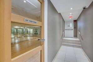 A hotel room with a wooden door, a sign indicating a hot yoga room, a staircase, and an exit sign.