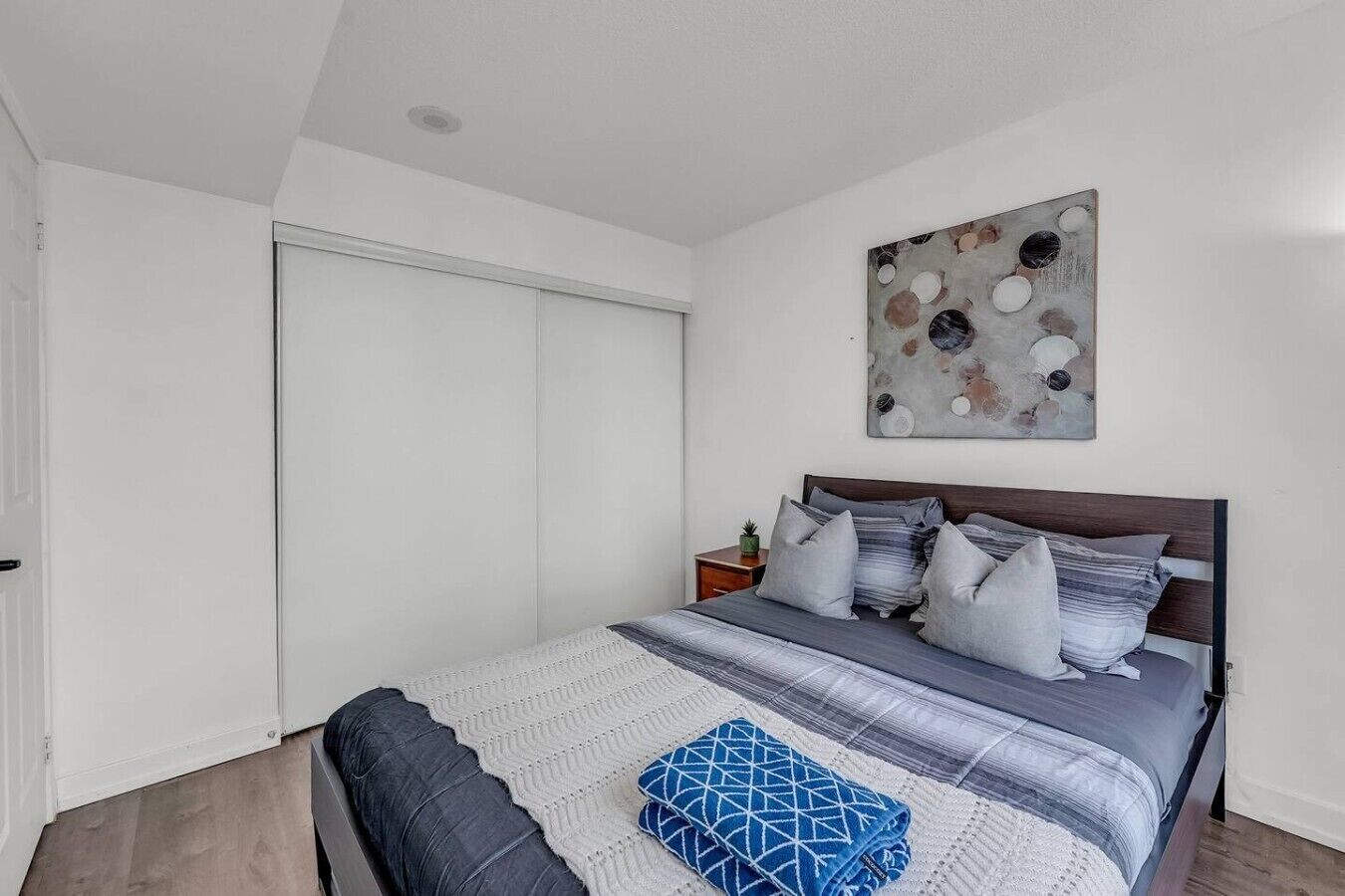 A bedroom with a bed, pillows, a blanket, a wall art piece, and a closed door.