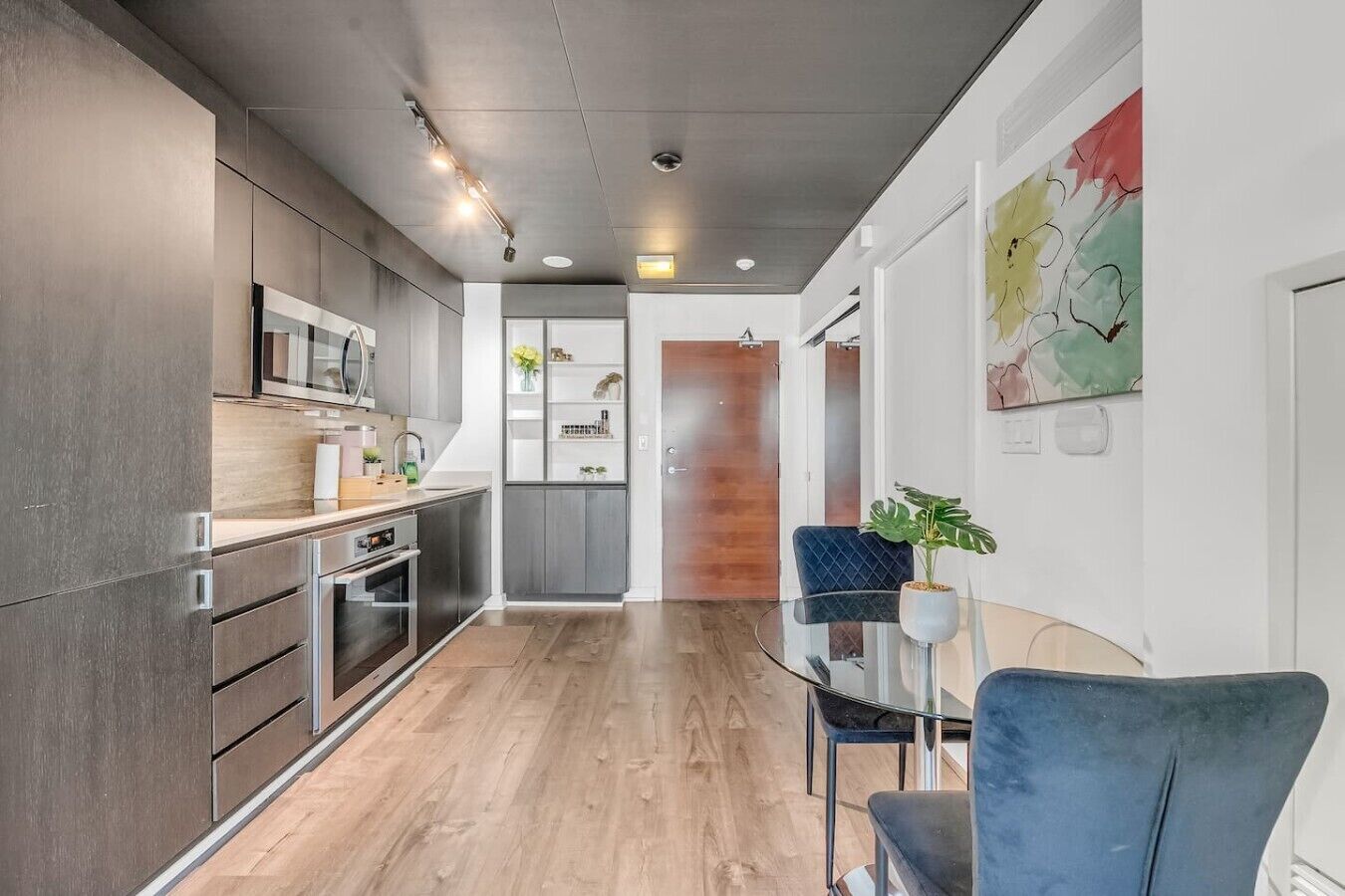 A modern kitchen with built-in appliances, a dining area with a glass table, and a view into a living space.