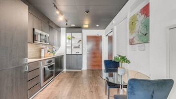 A modern kitchen with built-in appliances, a dining area with a glass table, and a view into a living space.