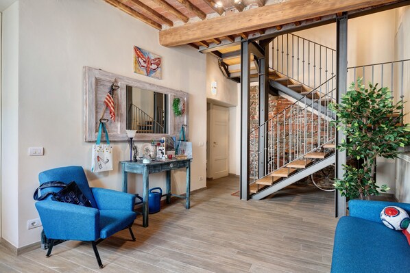 A living room with a blue sofa, a coffee table, a staircase with a metal railing, and a potted plant.
