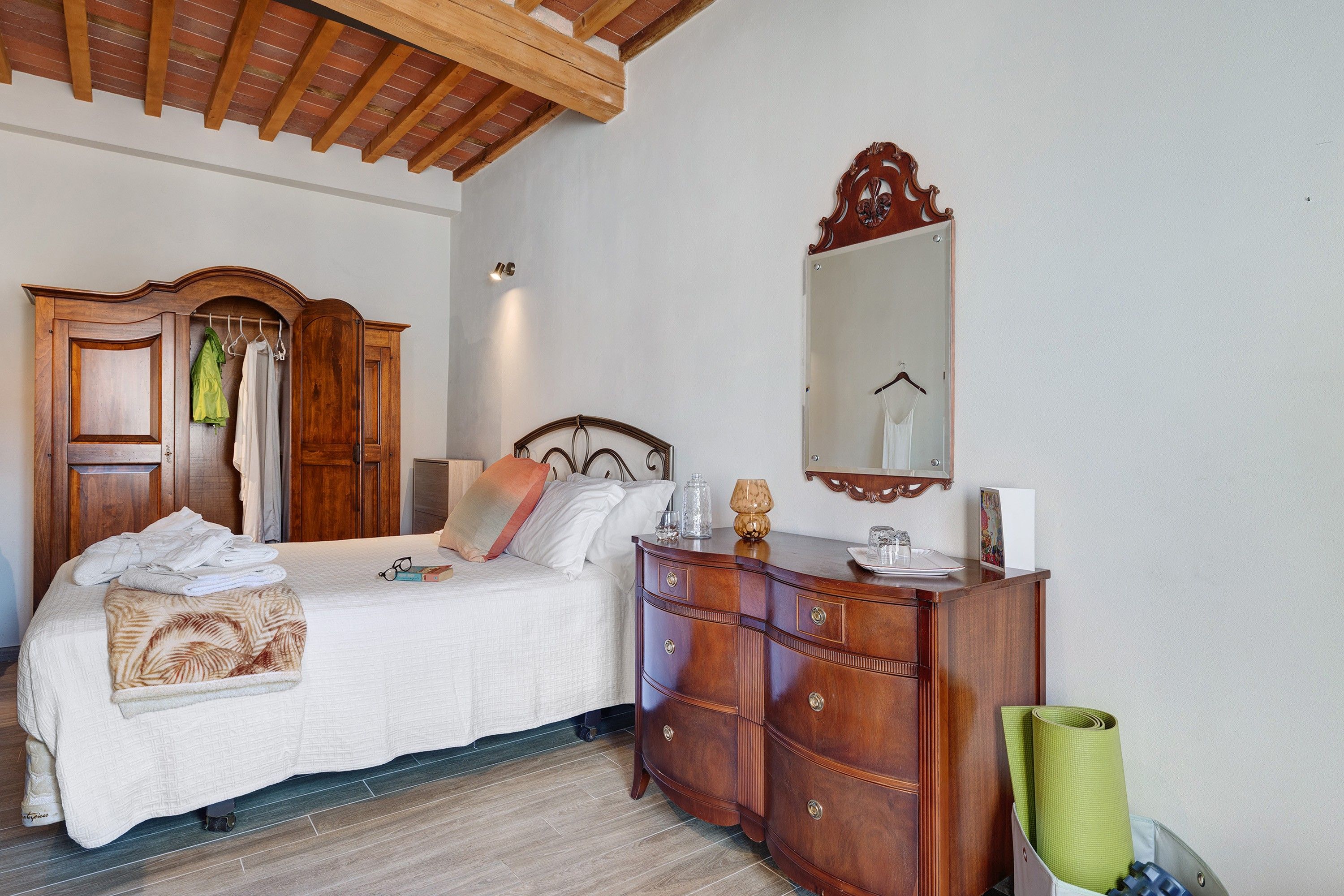 Een slaapkamer met een bed, een houten garderobe en een spiegel aan de muur.