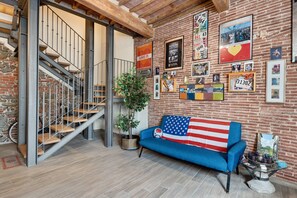 Een loft-achtige woonruimte met een trap, een blauwe bank versierd met een Amerikaanse vlag, en een bakstenen muur versierd met diverse ingelijste herinneringen.