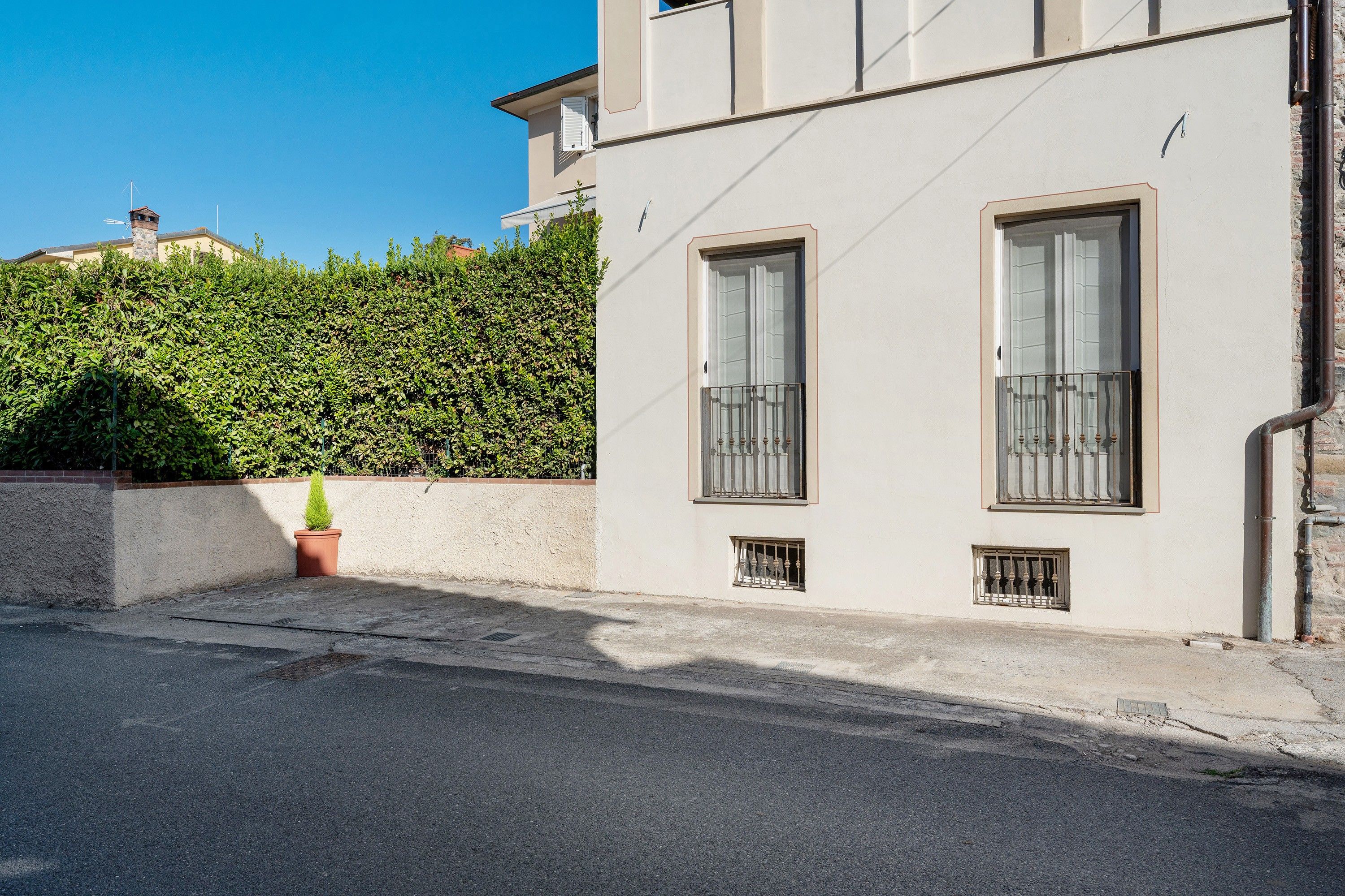 Ein Gebäude mit zwei Fenstern, einem kleinen Balkon und einer Hecke im Hintergrund.