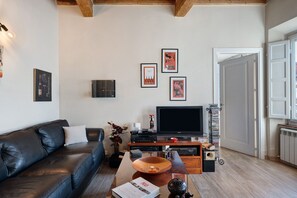 Een woonkamer met een leren bank, een flatscreen televisie, een salontafel met decoratieve items en ingelijste foto's aan de muur.