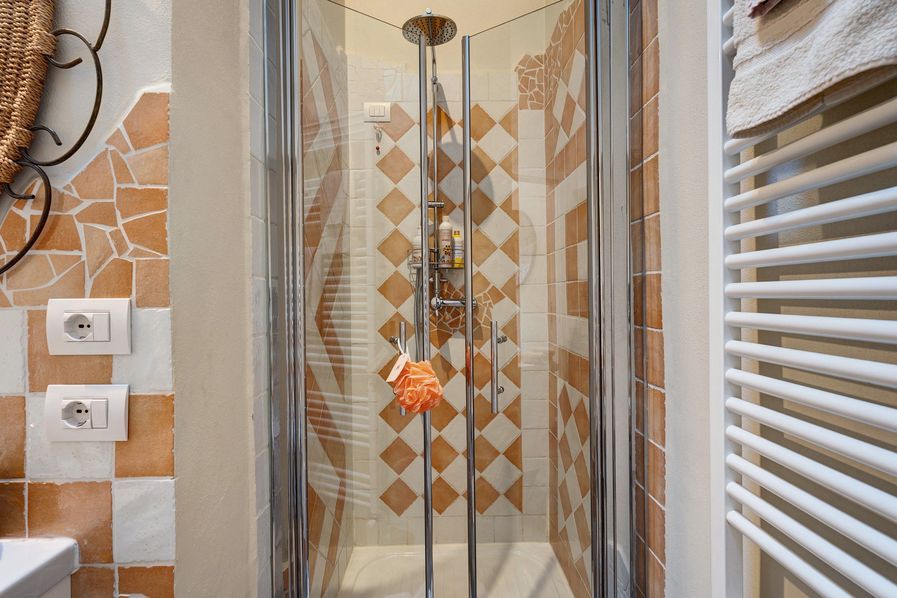 A shower with a glass door, a towel rack, and a patterned wall.
