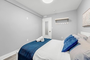 A bedroom with a bed, a door, a light fixture, and a wall-mounted shelf.
