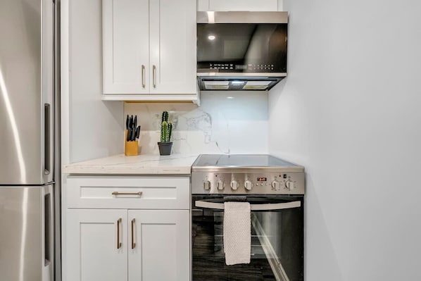 A kitchen with white cabinets, a stainless steel refrigerator, a stove, and a microwave.
