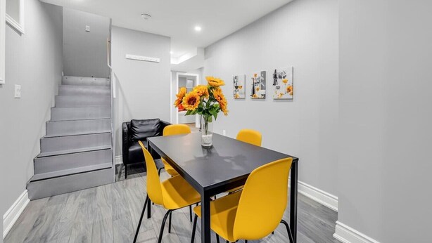 A modern dining area with a staircase, a table with yellow chairs, and a vase of sunflowers. - *Minutes to BMO Field* 3BR Home in Downtown (Toronto)