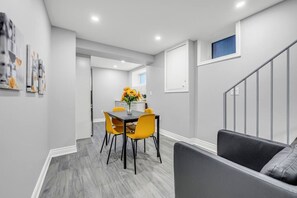 A modern interior with a dining area featuring a table and chairs, a sofa, and a staircase.